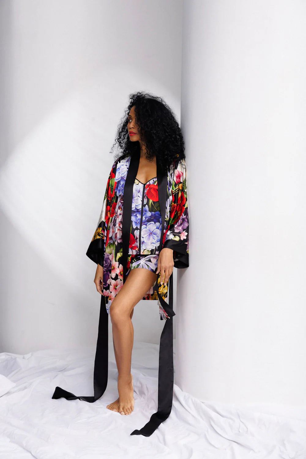 Woman wearing a colorful floral silk kimono with a matching set of camisole and shorts (sold separately) with long black belt. Showing the front full picture.